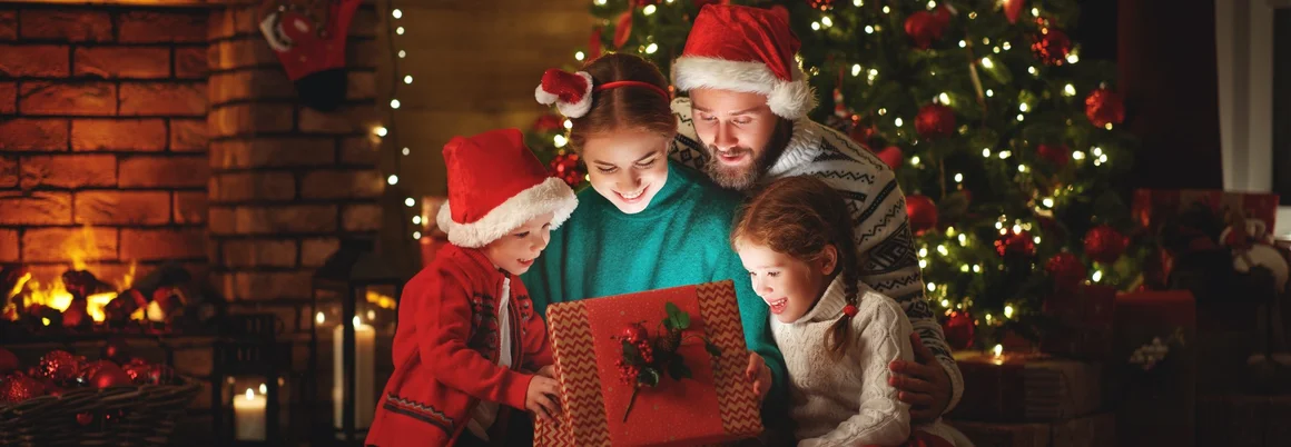 Familie öffnet Geschenk unterm Weihnachtsbaum